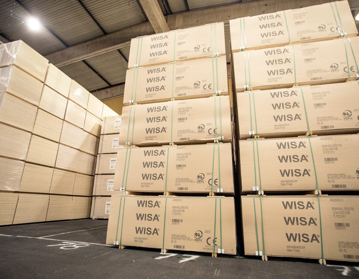 Höga staplar av kartonger märkta med "WISA" står uppradade i en lagerlokal. Golvet är klart och taket är av metall.