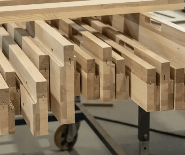 Långa träbitar med precisionsskärningar ligger på en arbetsbänk i en snickeriverkstad.