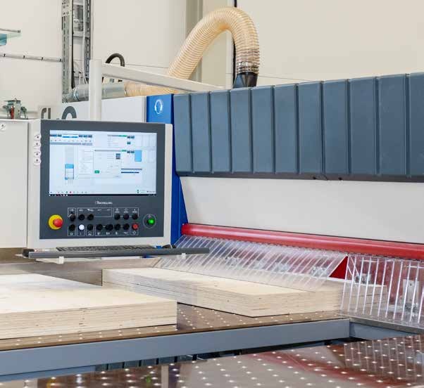 En industrimaskin i en verkstad med en digital skärm och kontrollpanel. Maskinen är utrustad med en stor arbetsyta för bearbetning av träskivor.